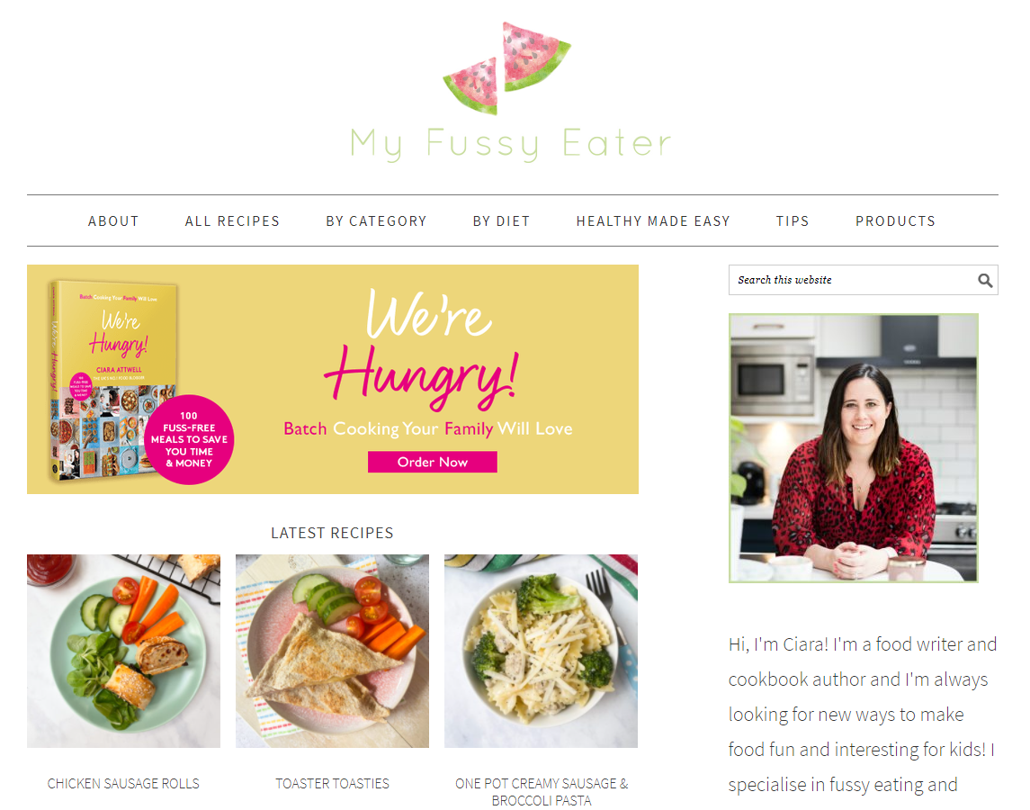 screenshot of the my fussy eater website which shows the logo, profile picture of the founder Ciara Attwell, various images of available recipes including chicken sausage rolls, toaster toasties and sausage and broccoli pasta, with an advertisement for a cookbook named 'we're hungry' displaying the cookbook itself